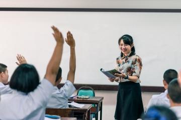 Teacher stood at front of class, students with hands up