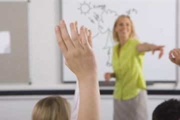 A confident looking teacher is surrounded by a sea of hands up from the class