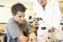 Teacher leaning over student, looking at a book with a microscope set up