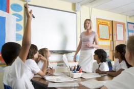 Teacher in front of whiteboard, backs of primary pupils with their hands up