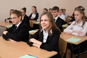 Girls sat at desk with arms folded in front of a row of orderly students